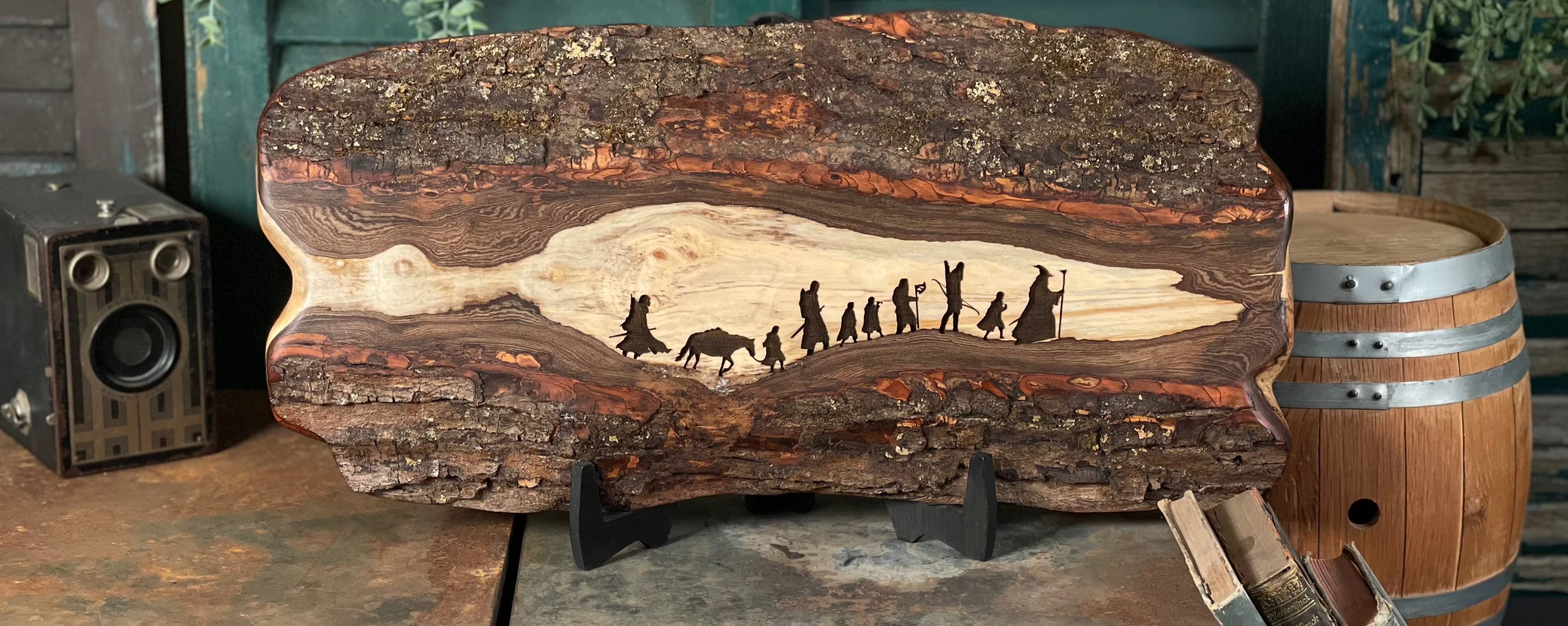 Wooden plaque with engraved scene of people and animals on a rustic setting with vintage furniture and barrel.
